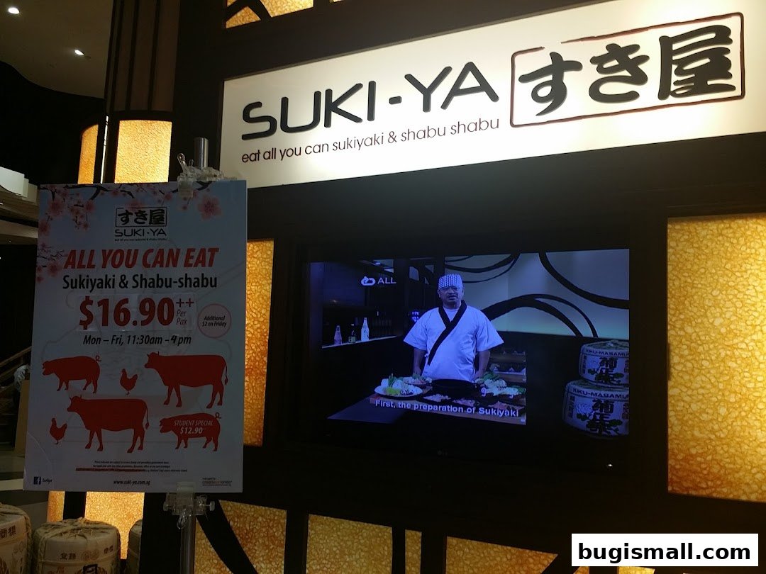 A sign advertising Suki-Ya's all-you-can-eat Sukiyaki and Shabu-shabu, with a TV screen showing food preparation.