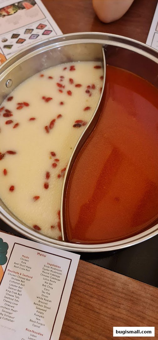 A split shabu-shabu pot with two different broths, alongside a menu.