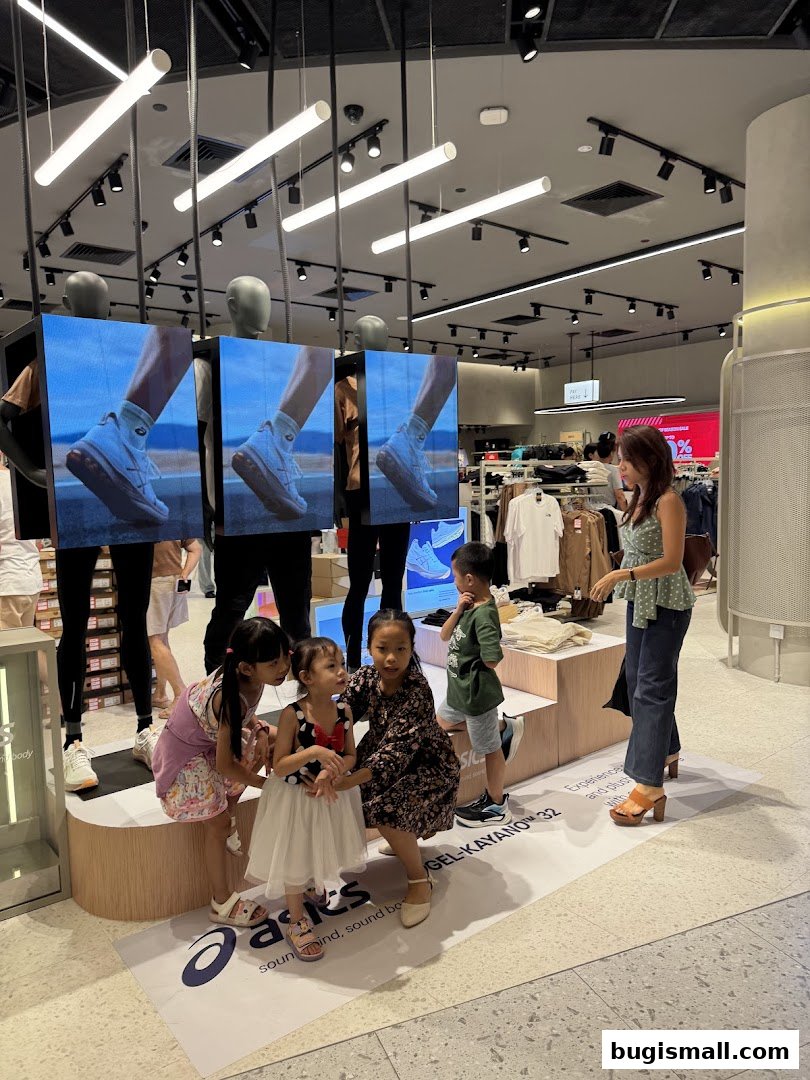 Children posing in front of Asics displays featuring shoes and clothing.