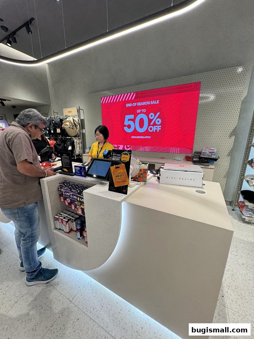 Customers at the counter of a sports store with a large screen advertising a sale.