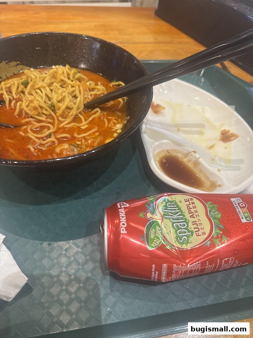 A bowl of ramen with chopsticks and a can of sparkling apple drink on a tray.