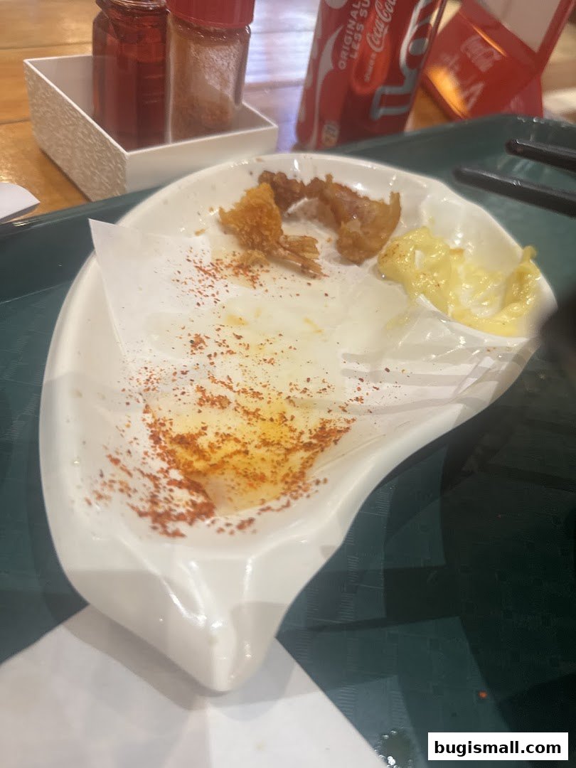 A plate with leftover fried shrimp, dipping sauce, and chili powder, next to a Coca-Cola can.