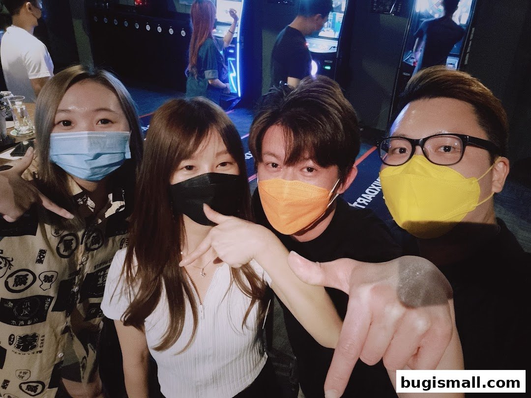 Four friends posing for a selfie in a dimly lit entertainment venue with dart machines in the background.