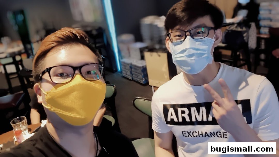 Two young men wearing face masks pose for a selfie inside a dimly lit establishment.