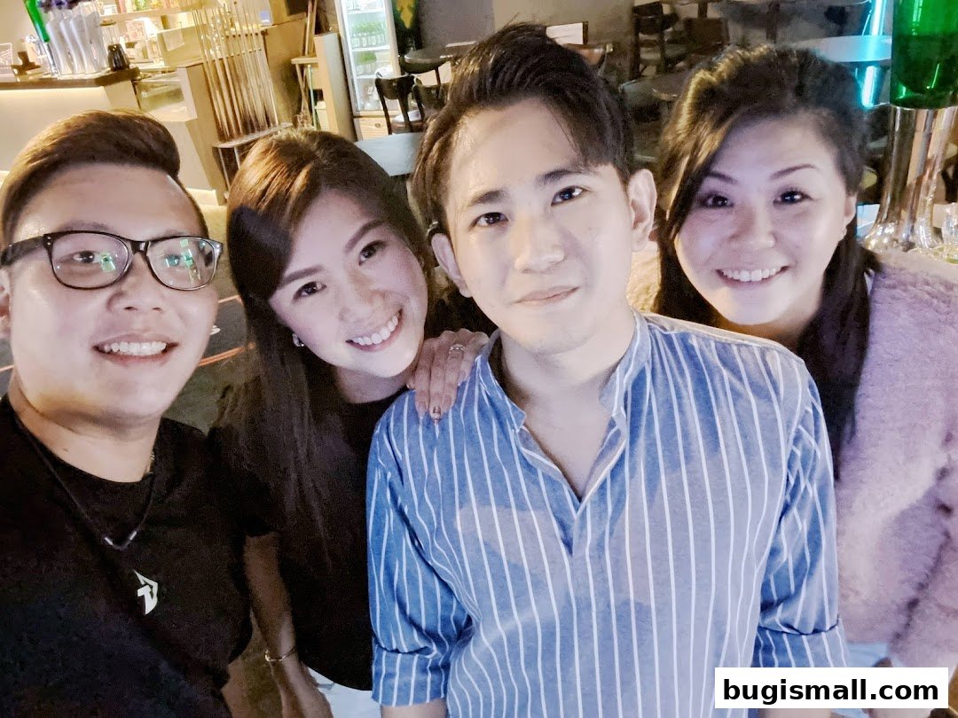 Four smiling friends pose for a selfie in a dimly lit venue with pool cues visible in the background.