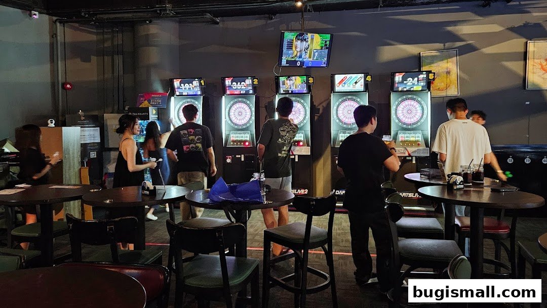 People playing darts at electronic dartboards in a bar setting with tables and chairs.
