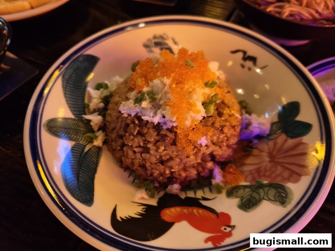 A close-up of a dish with rice, crab meat, and tobiko on a decorative plate.