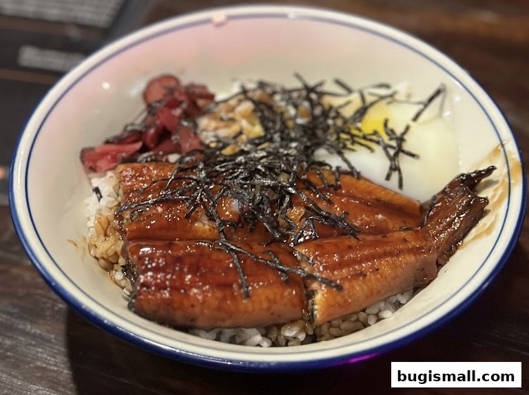 A close-up of a delicious bowl of unagi don with rice, topped with seaweed and pickled ginger.