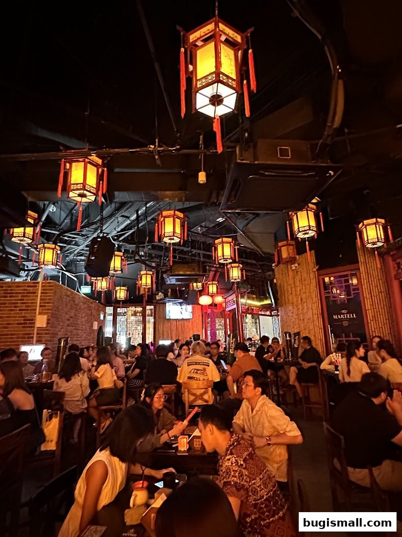 A lively indoor scene with many people dining and socializing under traditional Chinese lanterns.