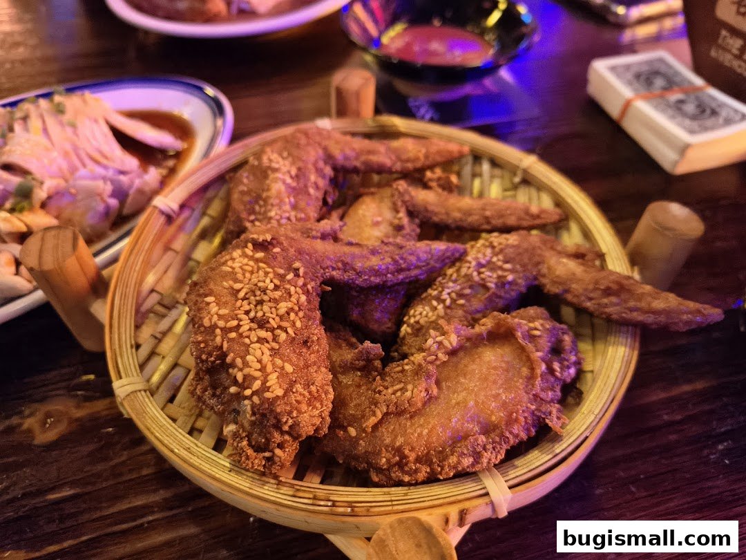 A basket of crispy fried chicken wings with sesame seeds, served with a side dish.