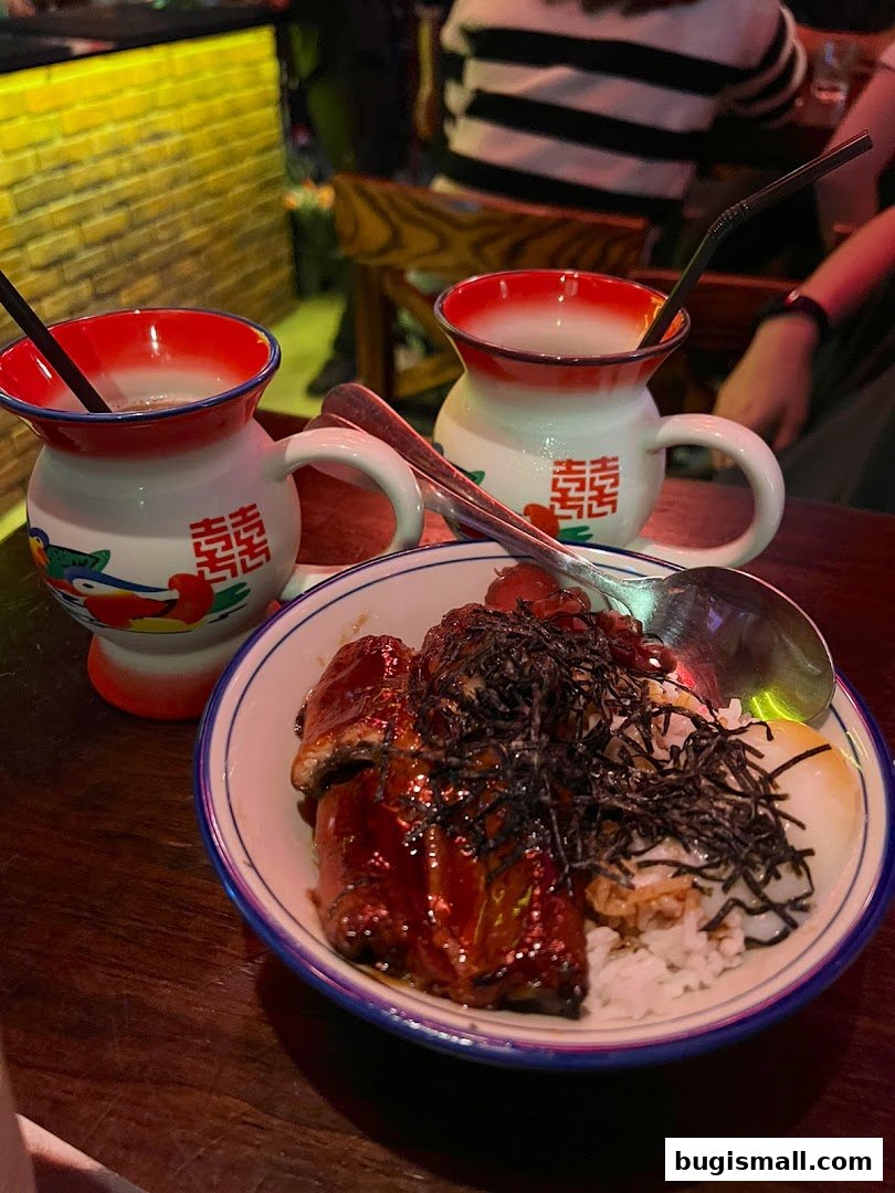 A bowl of rice with eel and a soft-boiled egg, served with two drinks.