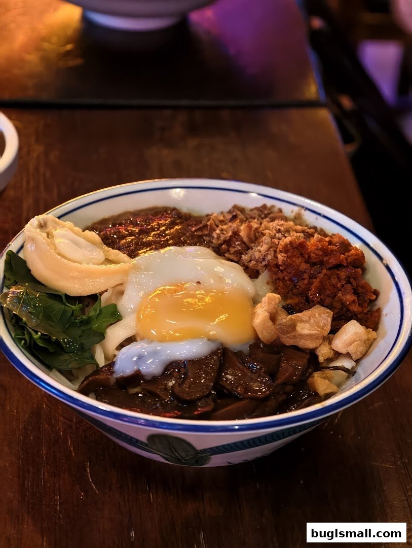 A close-up of a delicious bowl of noodles with a fried egg and various toppings.