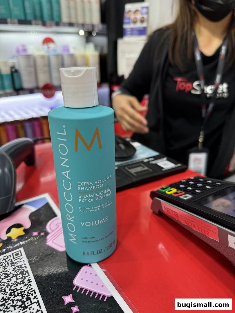 A bottle of Moroccanoil shampoo is displayed on a red counter with a payment terminal.