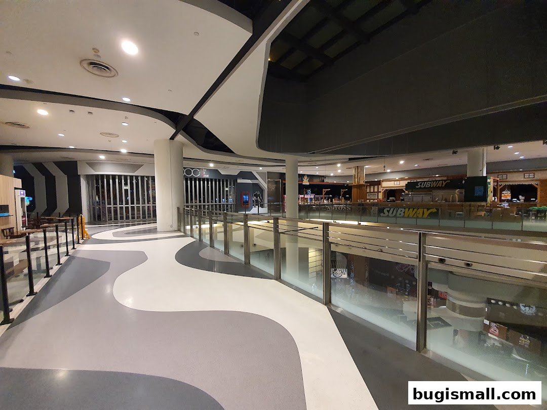 A modern shopping mall interior with a winding walkway and various shops visible on the upper level.