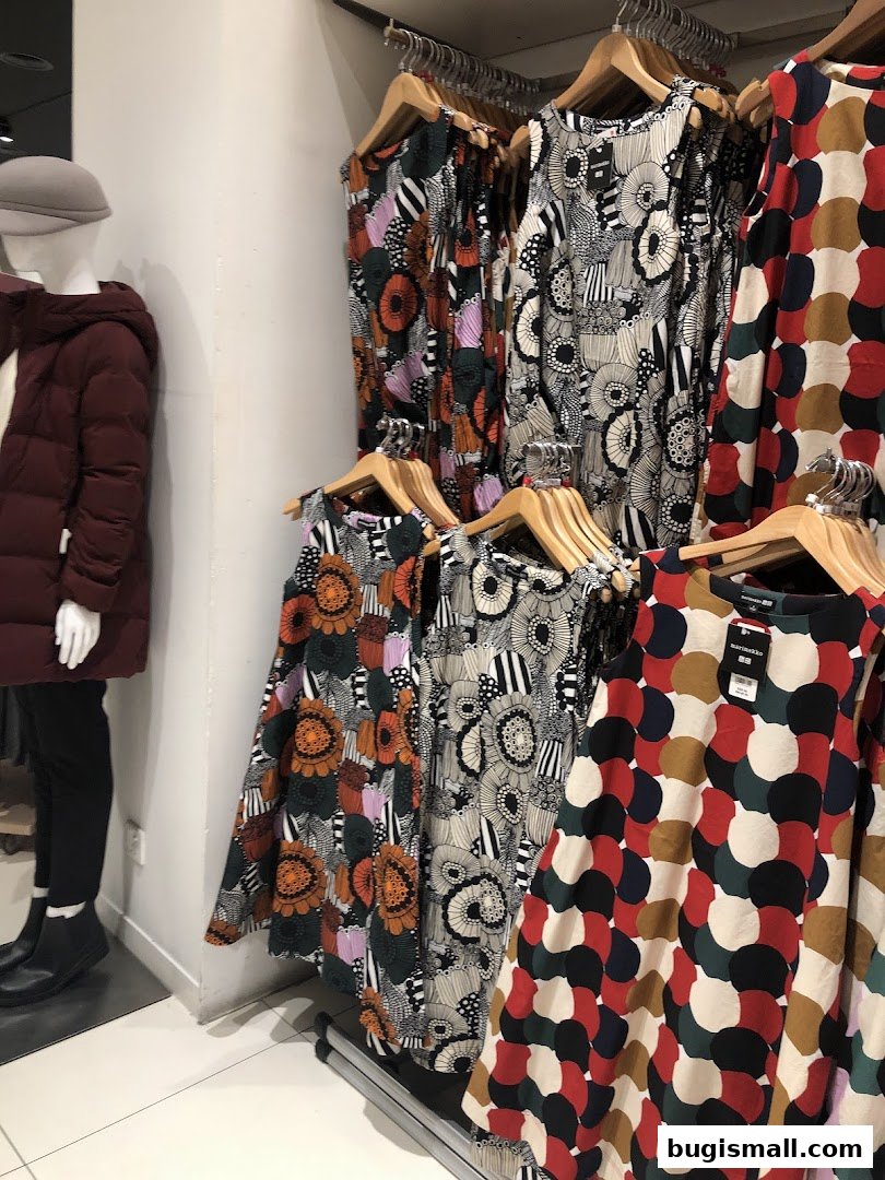 Mannequin in a maroon jacket and display of colorful patterned dresses.