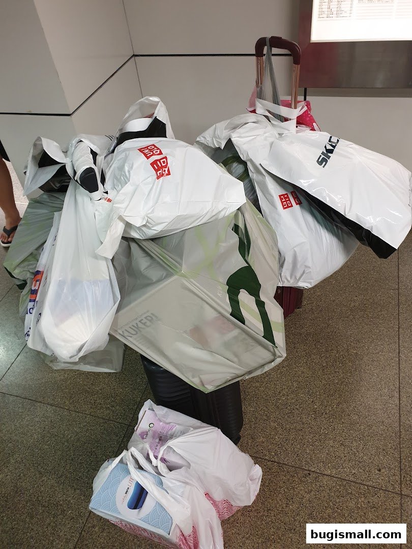 A collection of shopping bags from various stores, including UNIQLO, piled on top of luggage.