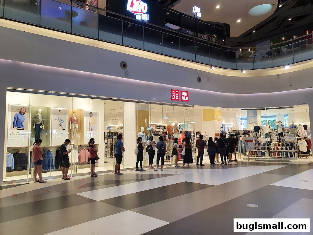 People queuing outside a brightly lit Uniqlo store in a shopping mall.