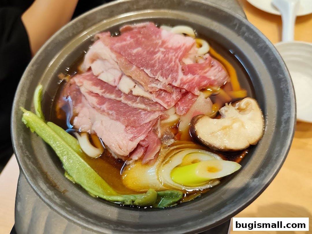 A close-up of a Japanese hot pot dish with thinly sliced beef, udon noodles, and vegetables.