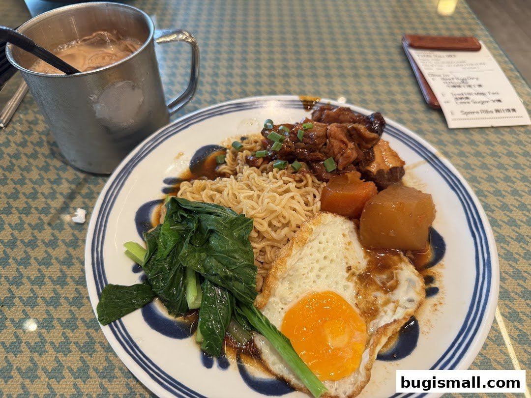 A plate of Hong Kong-style noodles with meat, vegetables, and a fried egg, alongside a drink.