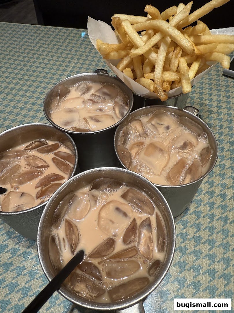 Four cups of iced milk tea and a basket of french fries on a patterned table.