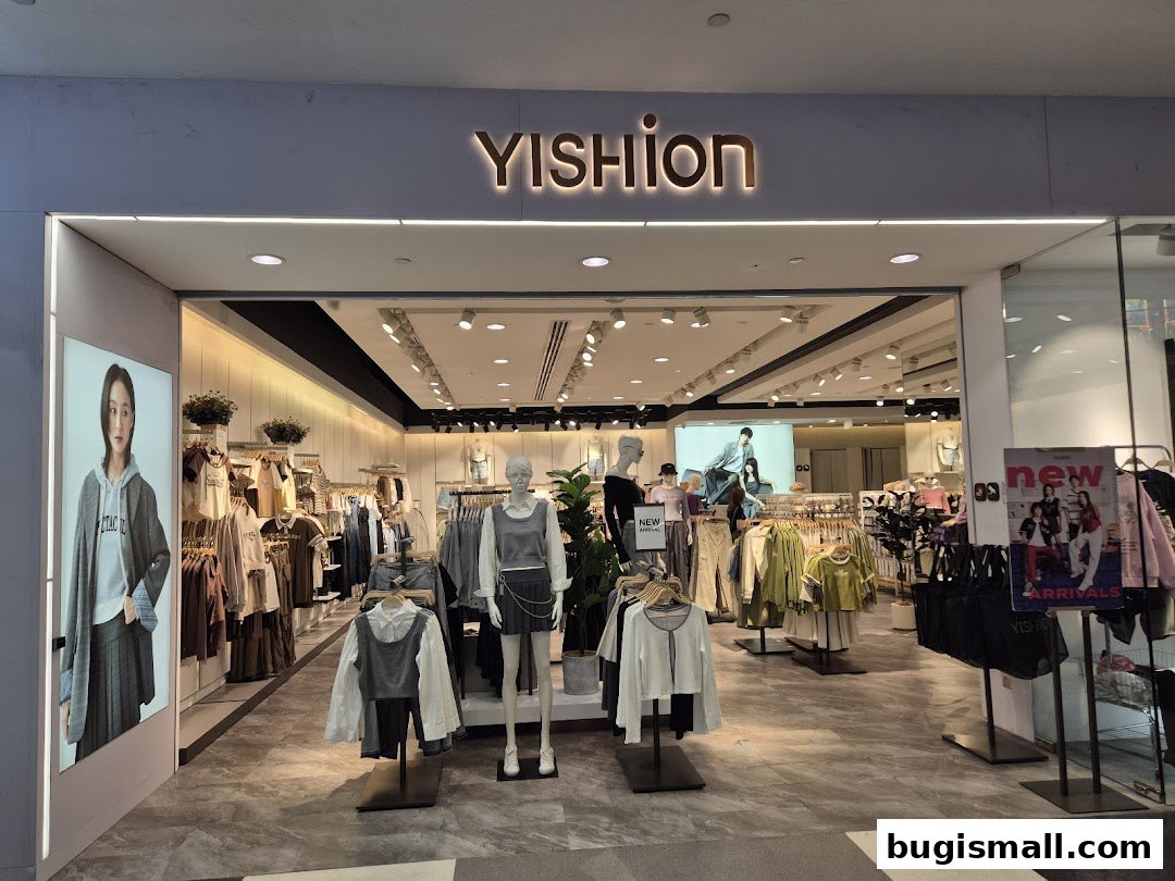 The YISHION Bugis shop front displays trendy apparel on mannequins and racks, with a large advertisement for new arrivals.