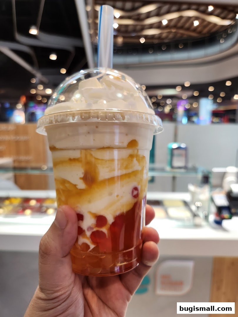 A hand holds a refreshing dessert drink with whipped cream and fruit pearls.