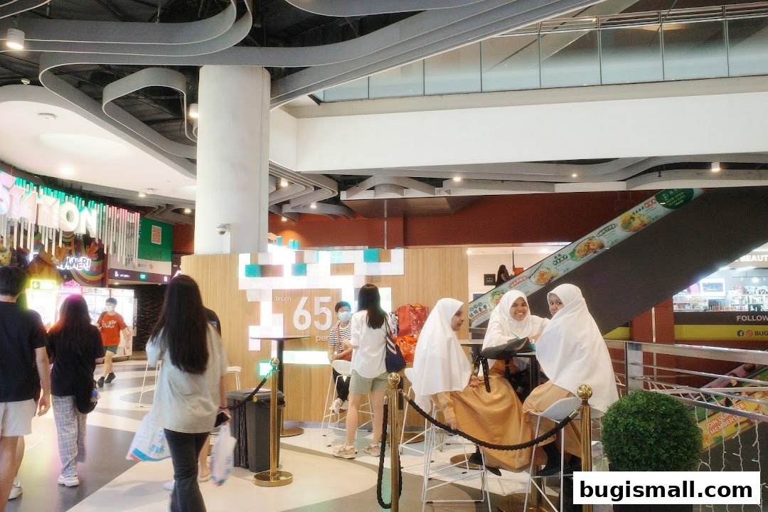 People are seated at tables in a brightly lit shopping mall with modern architecture.
